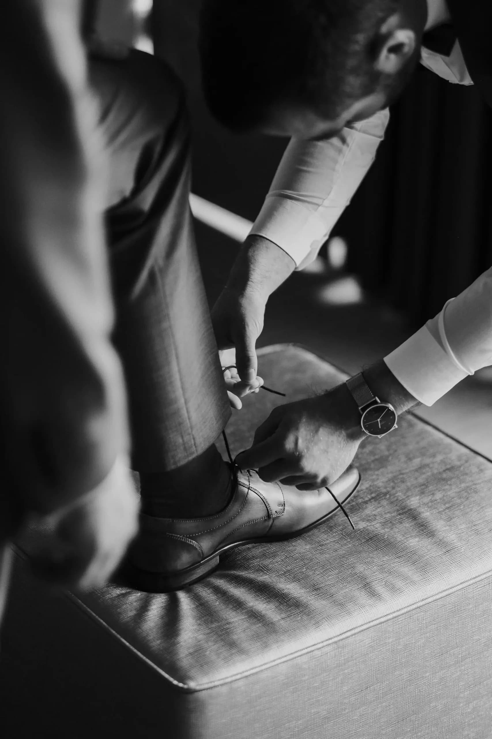 Schwarzweiß-Aufnahme zweier Personen in formeller Kleidung, Blick auf Schuhe und Armbanduhr